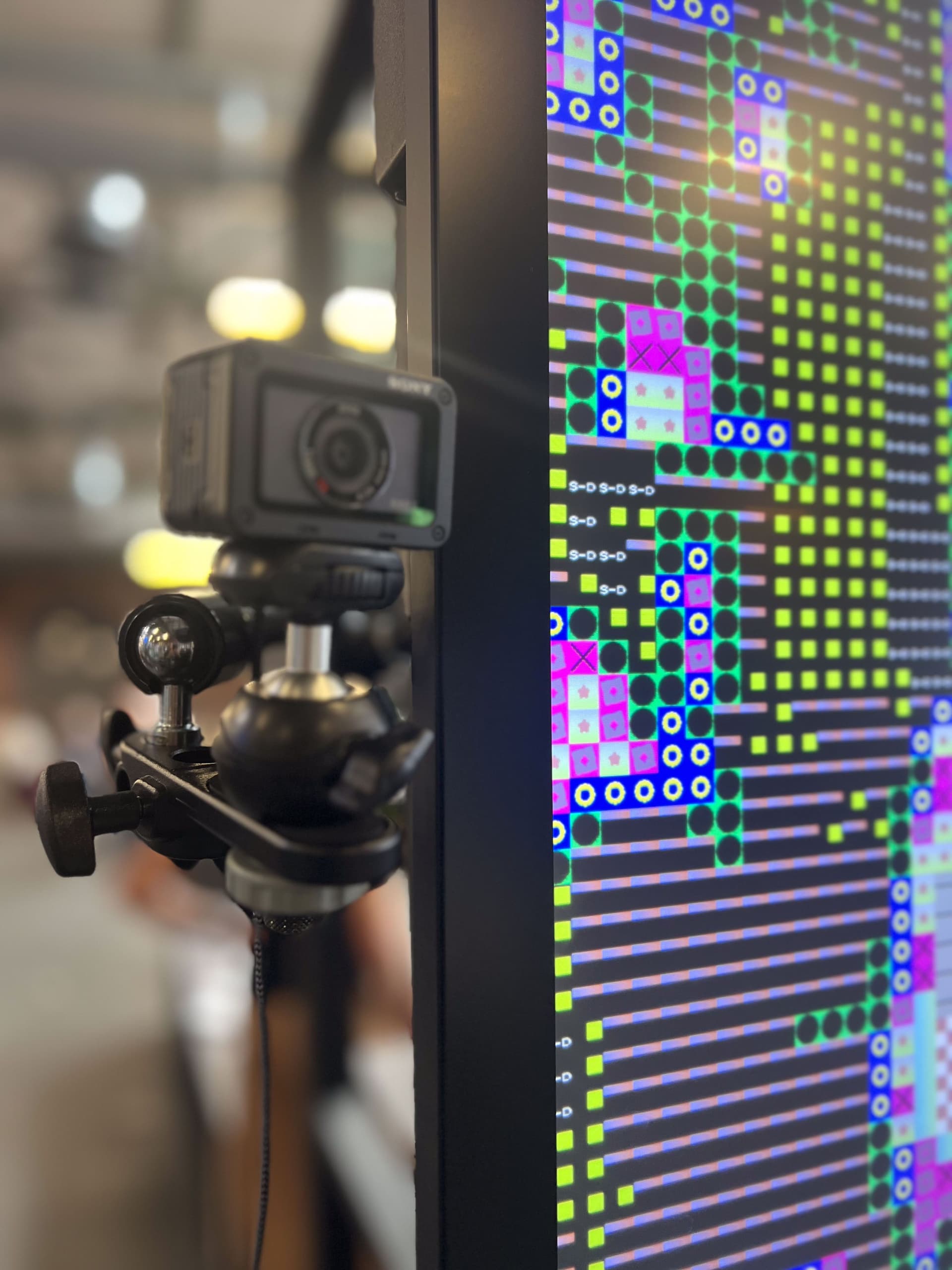 Camera on tripod next to a screen showing generative data visualization from the Identity Mirror installation